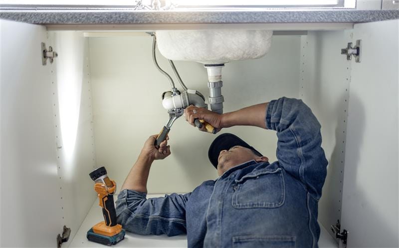 Plumber repairing pipes beneath a bathroom sink in Glendora
